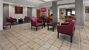 A hotel lobby with red leather chairs, a stone accent wall, a digital screen, and a reception desk. - Red Roof Inn & Suites Monroe, NC (Monroe)