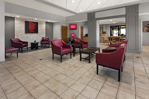 A hotel lobby with red leather chairs, a stone accent wall, a digital screen, and a reception desk. - Red Roof Inn & Suites Monroe, NC (Monroe)