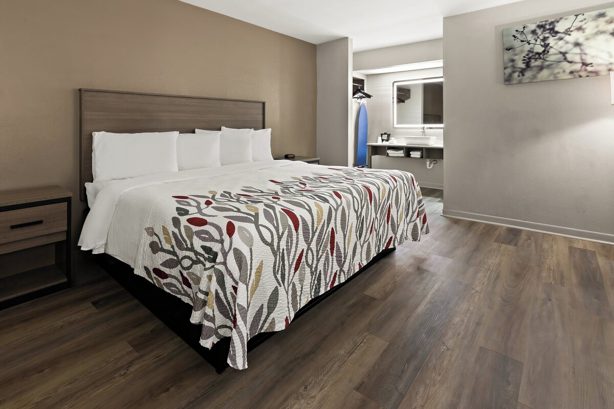 A neatly made bed with a patterned bedspread, a wooden headboard, and a nightstand with a drawer.