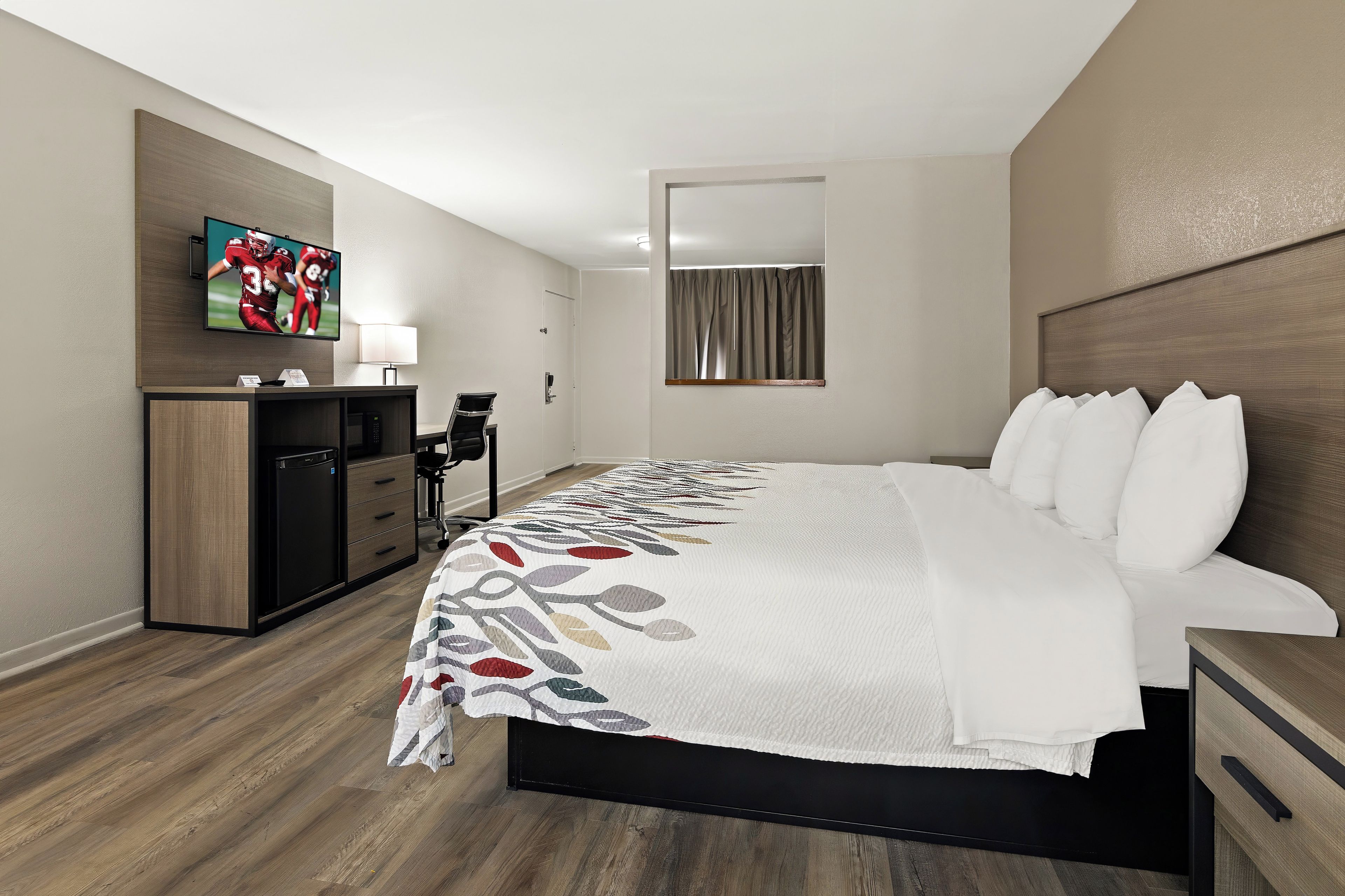 Een hotelkamer met een bed, een televisie, een bureau en een spiegel.