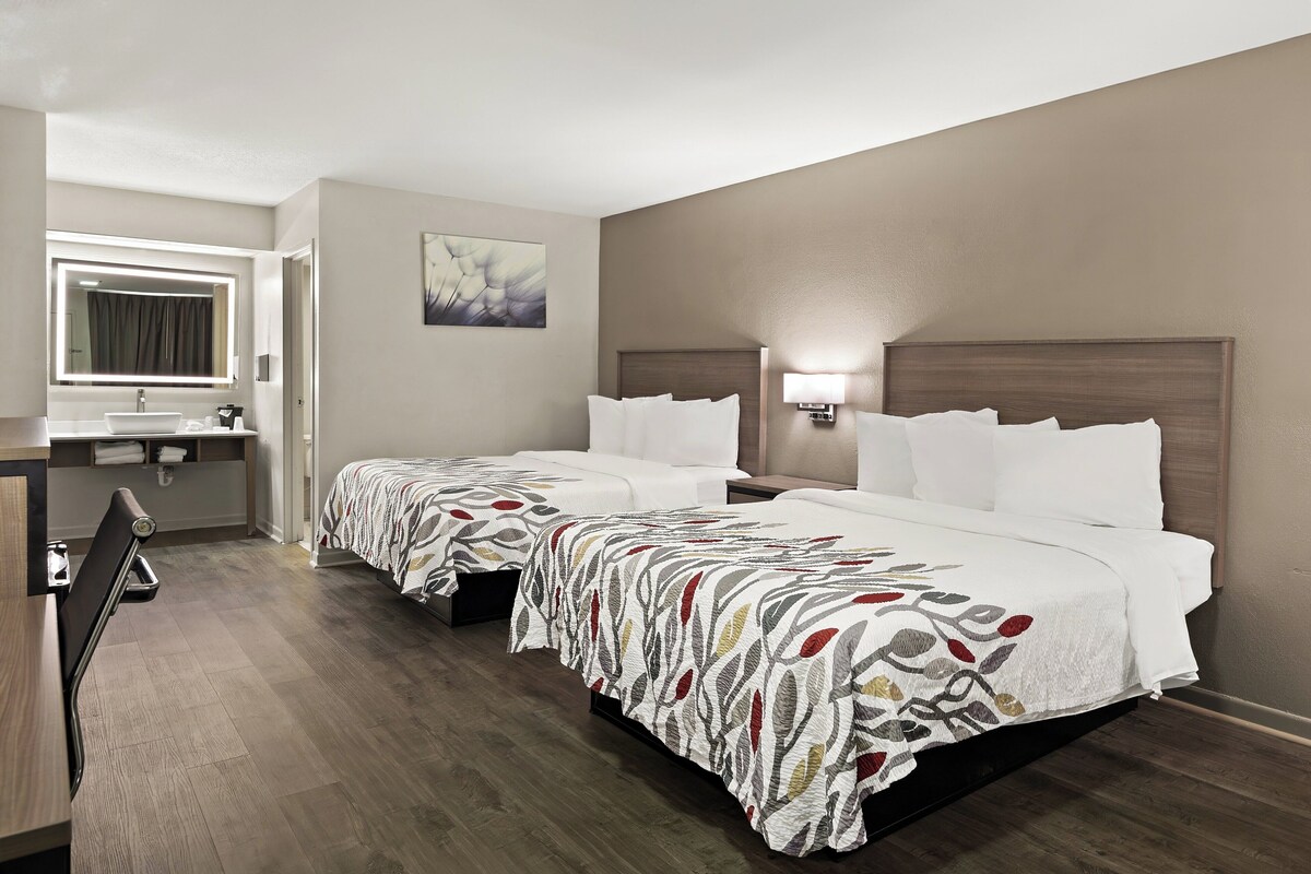 A hotel room with two beds, a bathroom, and a desk.