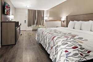 Habitación de hotel con una cama grande, un escritorio con televisión, una silla y una ventana con cortinas.