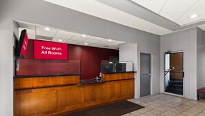 A reception area with a wooden desk, a red sign indicating free Wi-Fi, and a tiled floor. - Red Roof Inn & Suites Monroe, NC (Monroe)