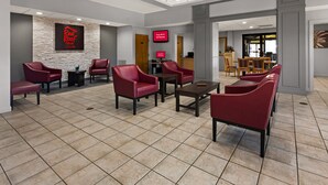 A hotel lobby with red leather chairs, a stone accent wall, a digital screen, and a reception desk. - Red Roof Inn & Suites Monroe, NC (Monroe)