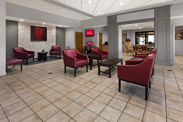 A hotel lobby with red leather chairs, a stone accent wall, a digital screen, and a reception desk. - Red Roof Inn & Suites Monroe, NC (Monroe)