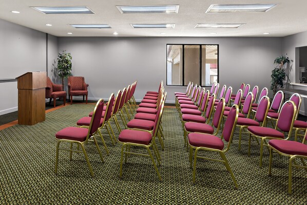 Un salón de conferencias con filas de sillas rojas y un atril, suelo alfombrado e iluminación en el techo.