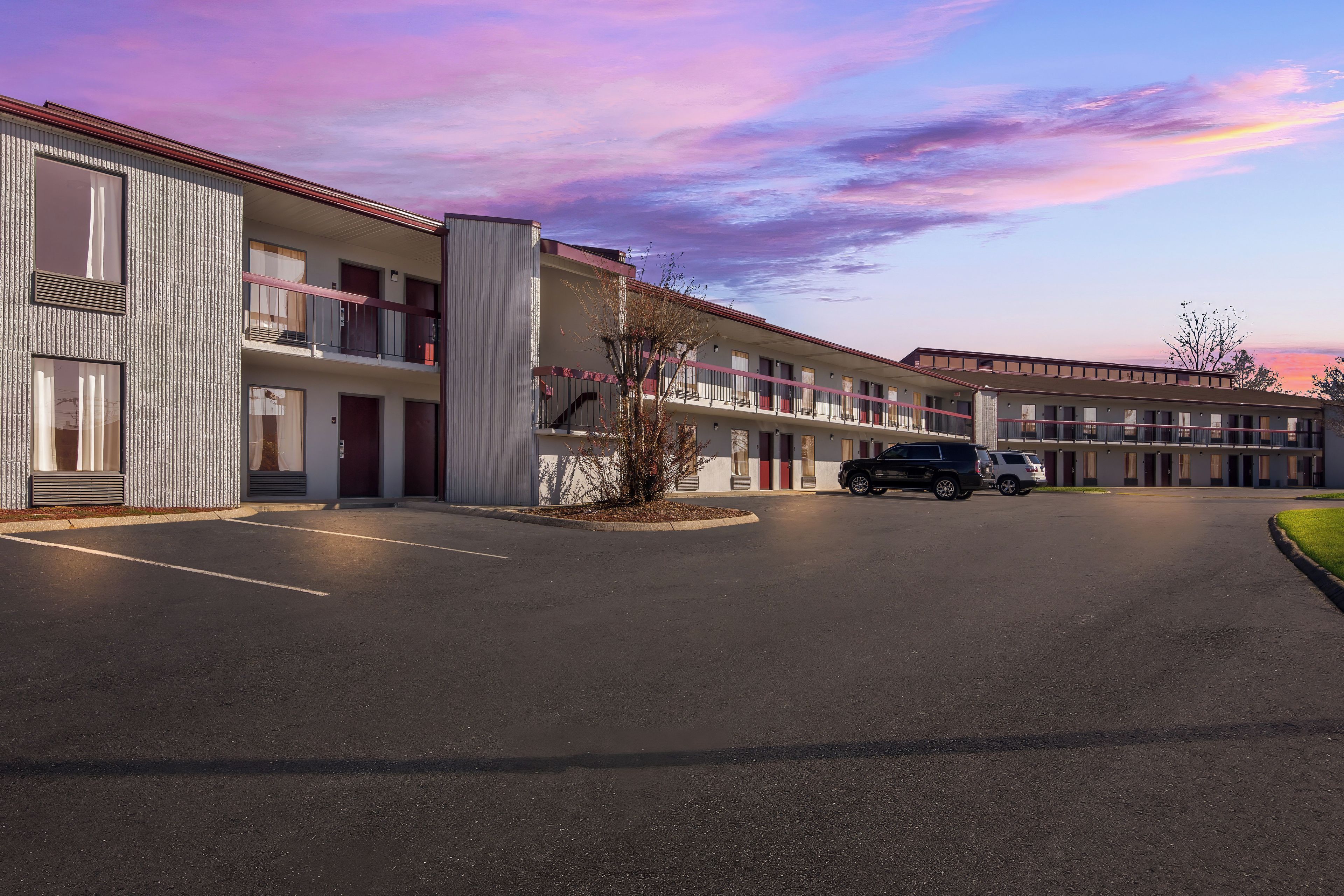 Un motel de varios pisos con estacionamiento, que presenta un diseño arquitectónico moderno con techo plano y una combinación de estilos de ventanas.