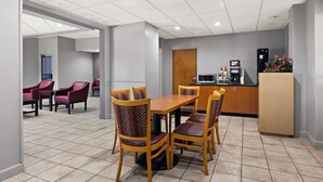 A hotel dining area with a wooden table and chairs, a kitchenette, and a seating area with red chairs. - Red Roof Inn & Suites Monroe, NC (Monroe)