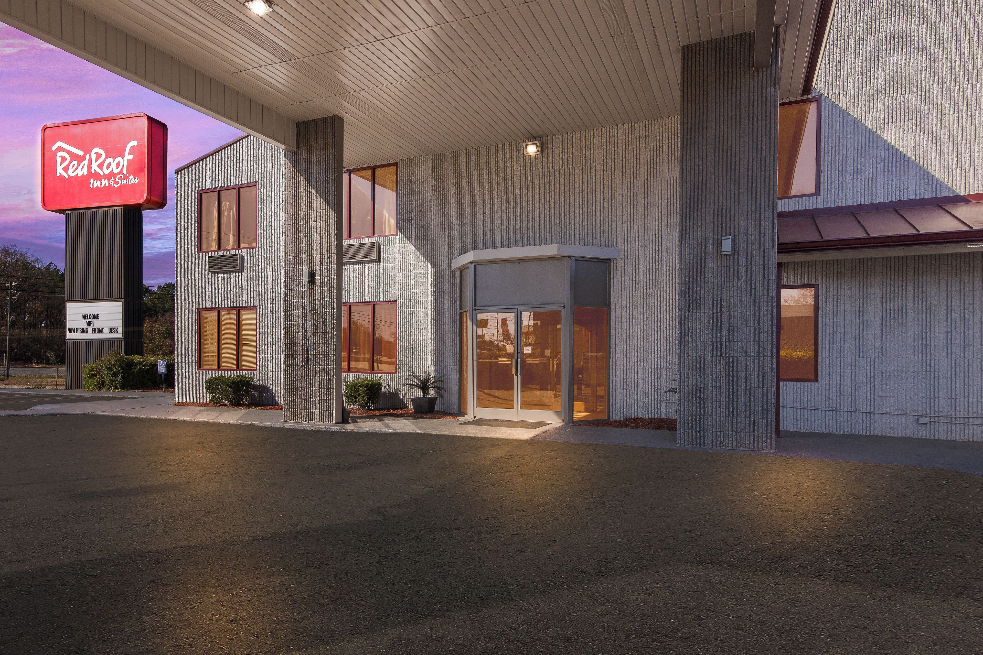 A Red Roof Inn & Suites with a modern design, featuring a prominent Red Roof sign, large windows, and a welcoming entrance.