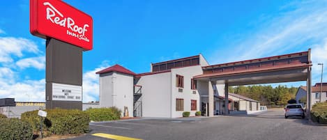 Un Red Roof Inn & Suites con cielo despejado, estacionamiento y un edificio con techo rojo.