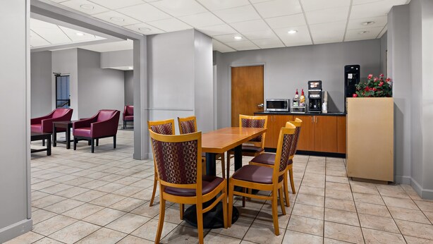 A hotel dining area with a wooden table and chairs, a kitchenette, and a seating area with red chairs. - Red Roof Inn & Suites Monroe, NC (Monroe)