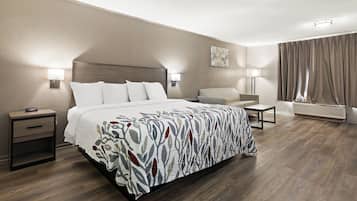 Une chambre d’hôtel avec un grand lit, des tables de chevet, une chaise, un bureau, une lampe et une fenêtre avec des rideaux.