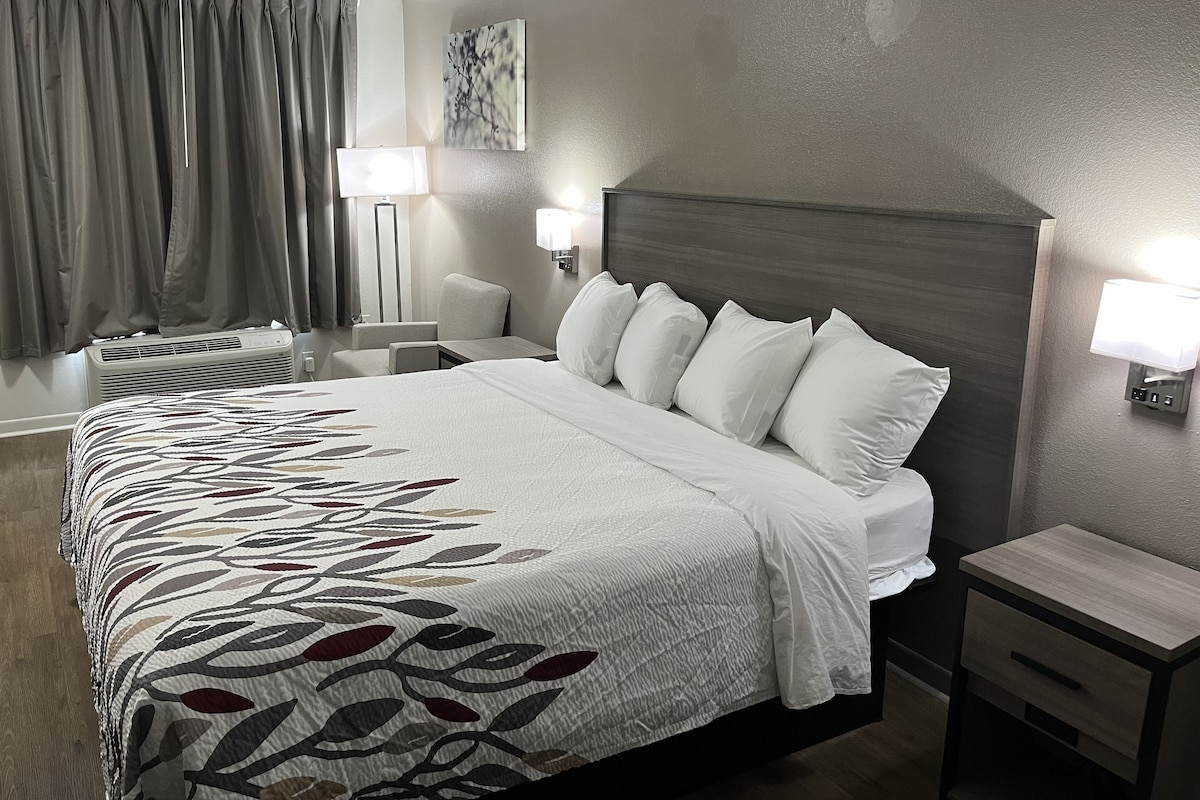 A hotel room with a large bed, two bedside tables, a wall-mounted lamp, and a ceiling fan.