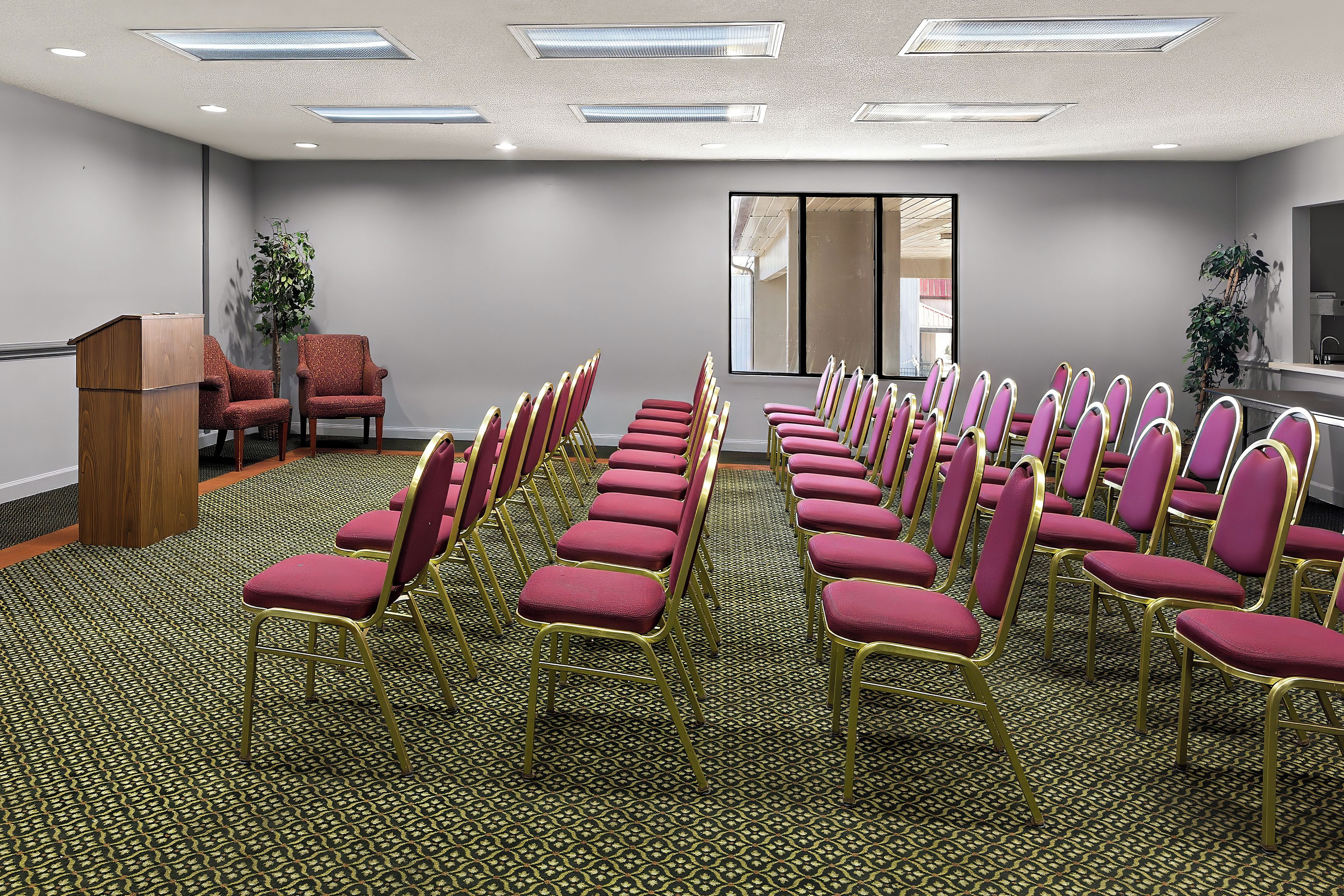 Un salón de conferencias con filas de sillas, un atril y un amplio ventanal.