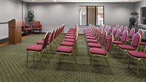 A conference room with rows of chairs, a podium, and a large window. - Red Roof Inn & Suites Monroe, NC (Monroe)