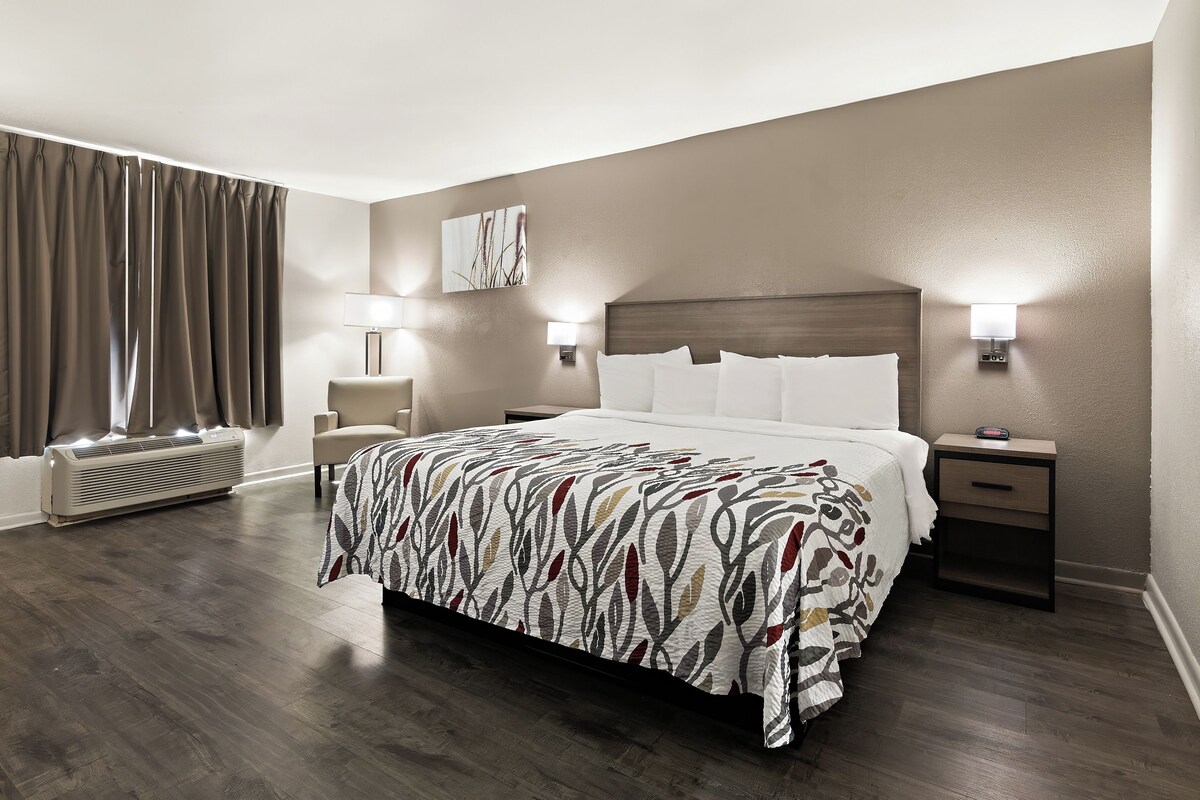 A hotel room with a large bed, two bedside tables with lamps, a wall-mounted heater, and a window with curtains.