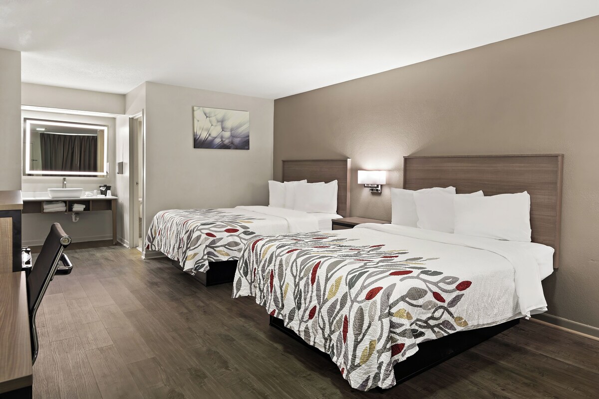 A hotel room with two beds, a bathroom, and a desk.