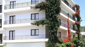 Un immeuble à plusieurs étages doté de balcons, une voiture garée devant et un arbre aux fleurs rouges.