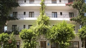 Un immeuble à plusieurs étages, doté de balcons, d’une entrée centrale et entouré de verdure.