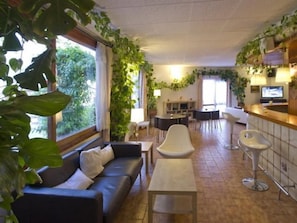 Une pièce comprenant un canapé, une table à manger et des chaises, un coin bar et de grandes fenêtres avec des rideaux.