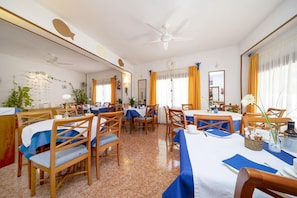 Un coin repas avec des chaises et des tables en bois, un ventilateur de plafond et un grand miroir au mur.