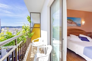 A balcony with a view of the city, a bed with white bedding, and a painting on the wall. - Manolita Hostal (Sant Antoni de Portmany)