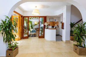 Un hall d’hôtel doté d’un comptoir d’accueil incurvé, d’un espace salon avec un canapé bleu et de plantes en pot.
