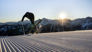 A skier on a snowy slope with mountains in the background and the sun shining.