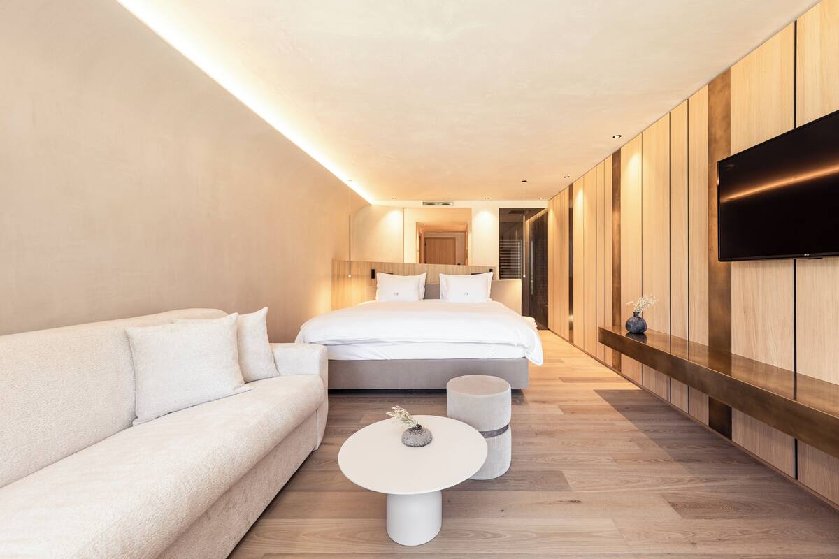 Une chambre d’hôtel moderne, dotée d’un grand lit, d’un canapé, d’une petite table ronde et d’un téléviseur fixé au mur.