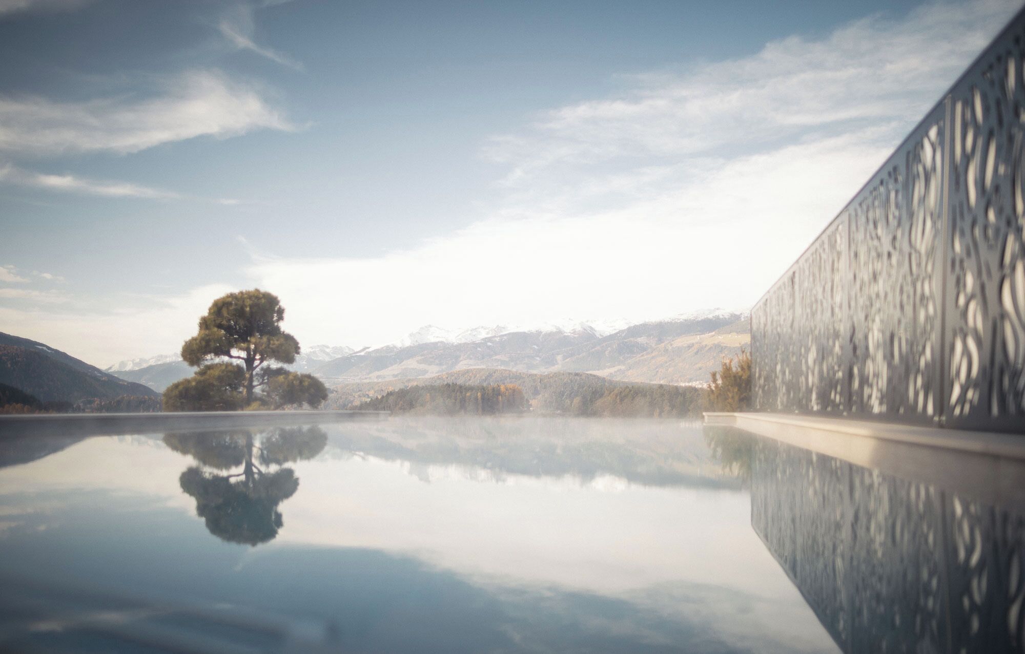 A serene landscape with a reflective water surface, a solitary tree, and distant mountains.