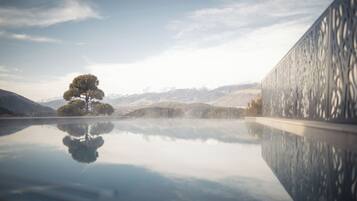 A serene landscape with a reflective water surface, a solitary tree, and distant mountains.