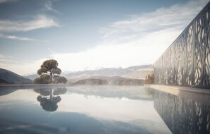 A serene landscape with a reflective water surface, a solitary tree, and distant mountains. - Hotel Winkler (San Lorenzo di Sebato)
