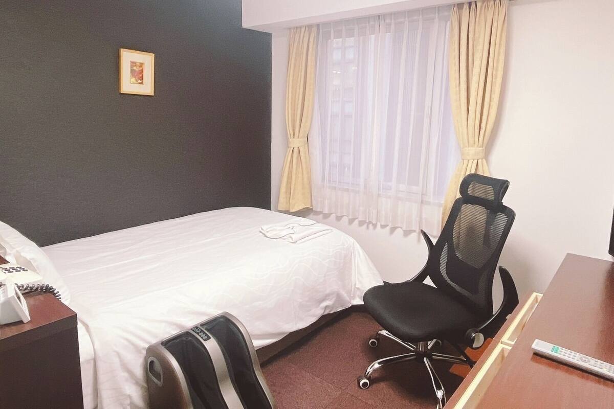 A hotel room with a bed, a desk, a chair, a telephone, and a window with curtains.