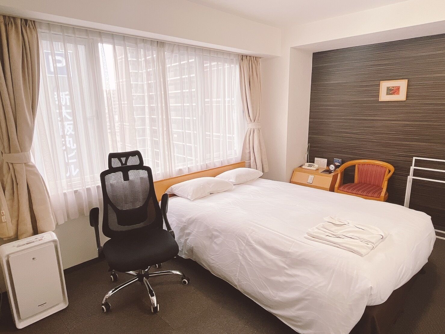 A hotel room with a bed, a desk, a chair, and a radiator.