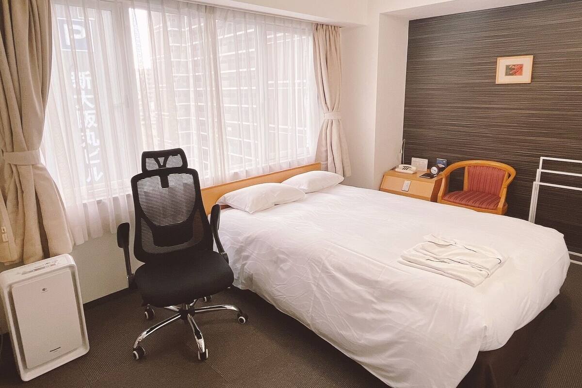 A hotel room with a bed, a desk, a chair, and a radiator.