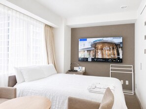 A hotel room with a bed, a TV mounted on the wall, a window with curtains, and a small table. - Hotel Shin Osaka (Osaka)
