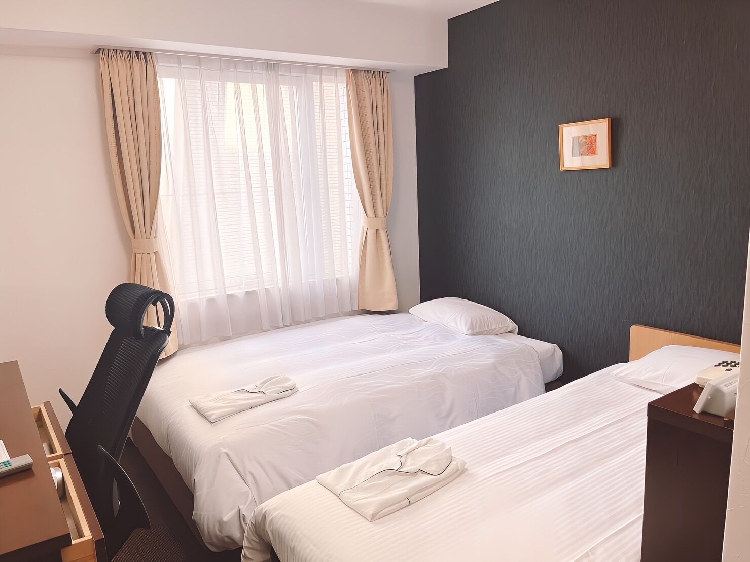 A hotel room with two beds, a desk, a chair, and a window with curtains.