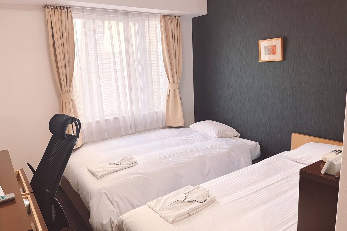 A hotel room with two beds, a desk, a chair, and a window with curtains.