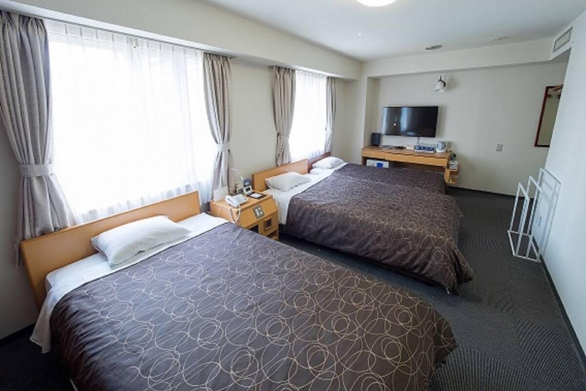 A hotel room with two beds, a TV, a desk, and a window with curtains.