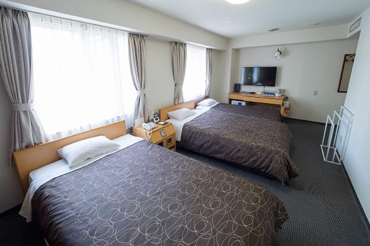 Habitació d'hotel amb dos llits, una televisió, un escriptori amb un ordinador i una finestra amb cortines.