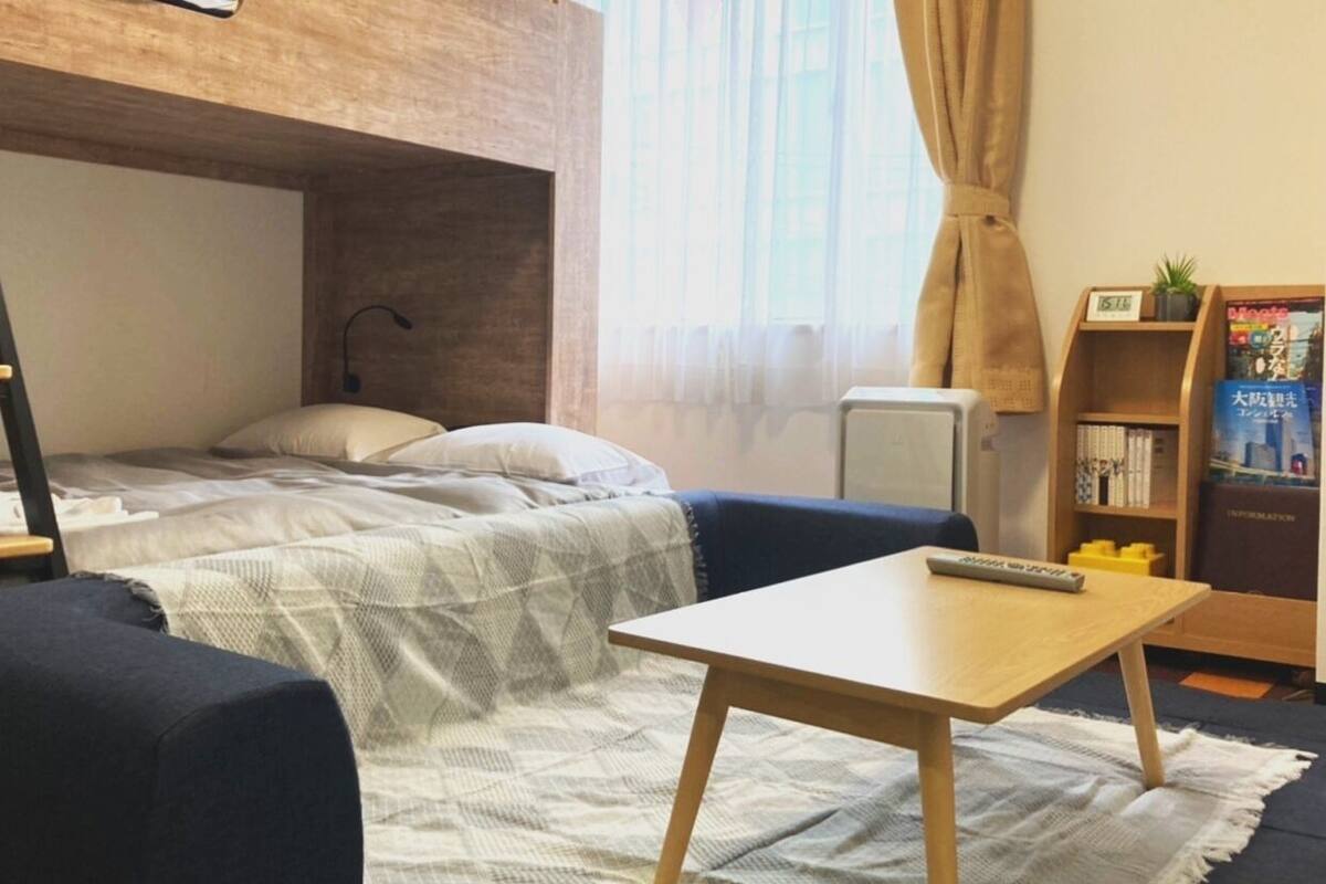 A bunk bed with a desk and chair, a bookshelf, and a window with curtains.