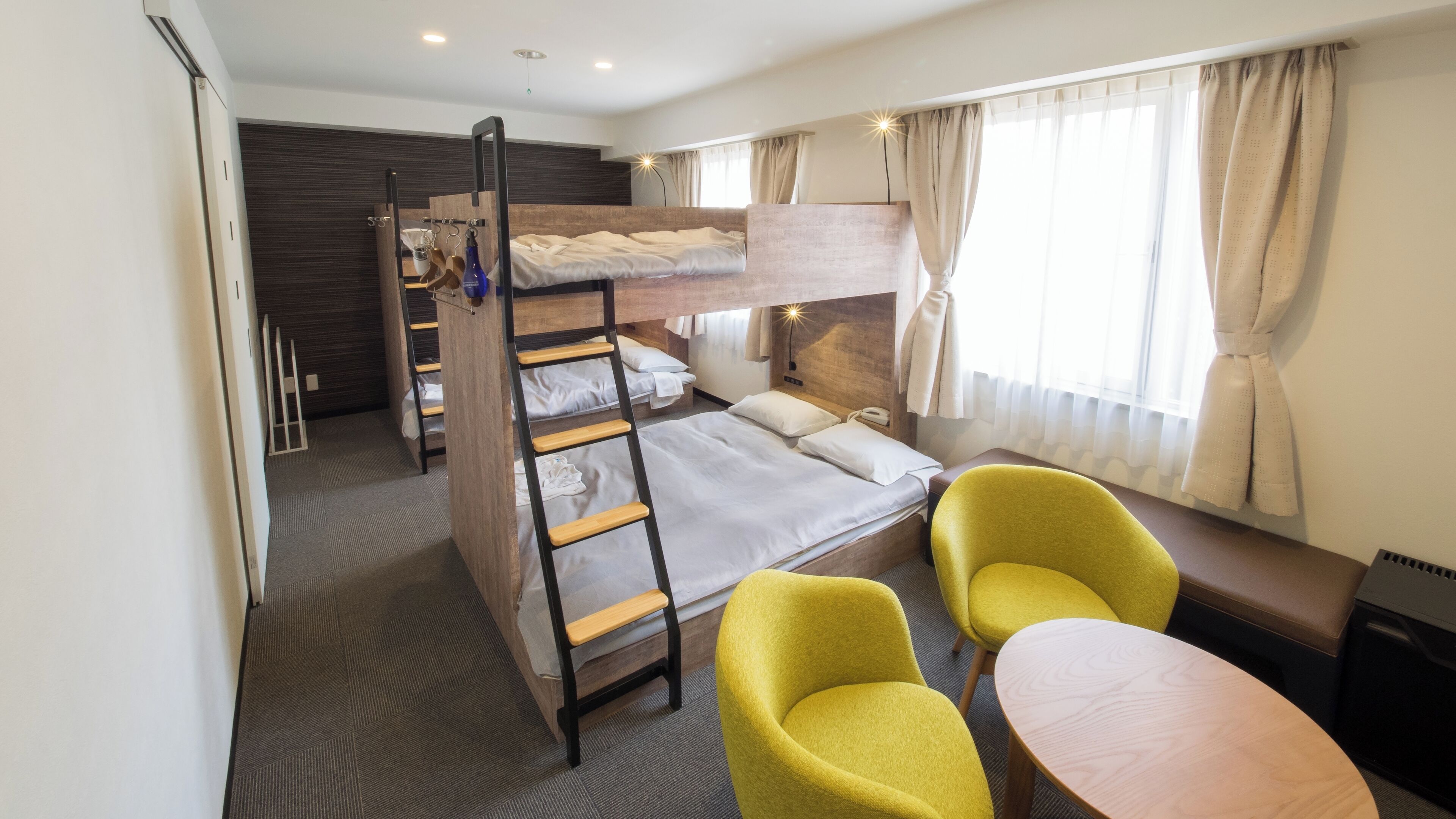 A bunk bed room with a ladder, a small table, two chairs, and a window with curtains.