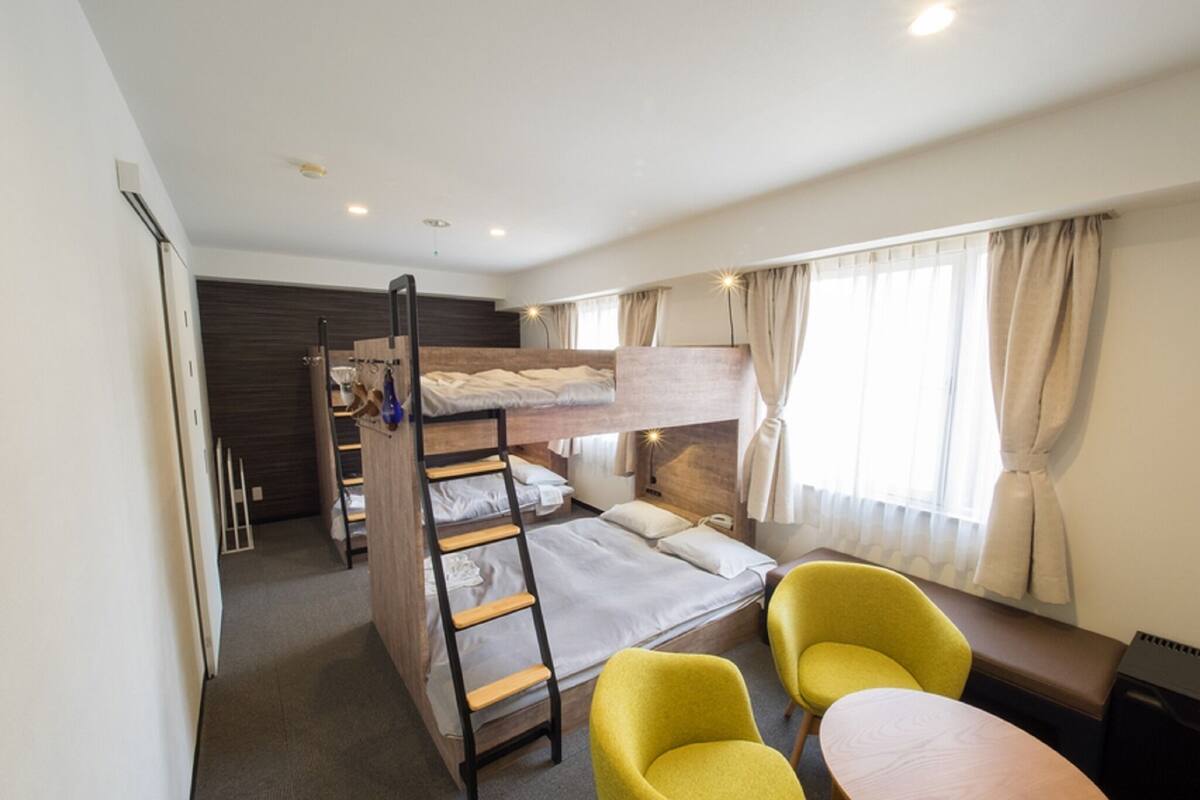 A room with bunk beds, a desk, two chairs, and a window with curtains.
