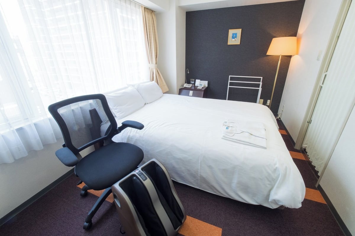 Habitació d'hotel amb llit, escriptori, cadira, làmpada i un quadre a la paret.
