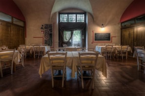Un comedor con mesas dispuestas para cuatro, sillas de madera y un gran ventanal con cortinas.