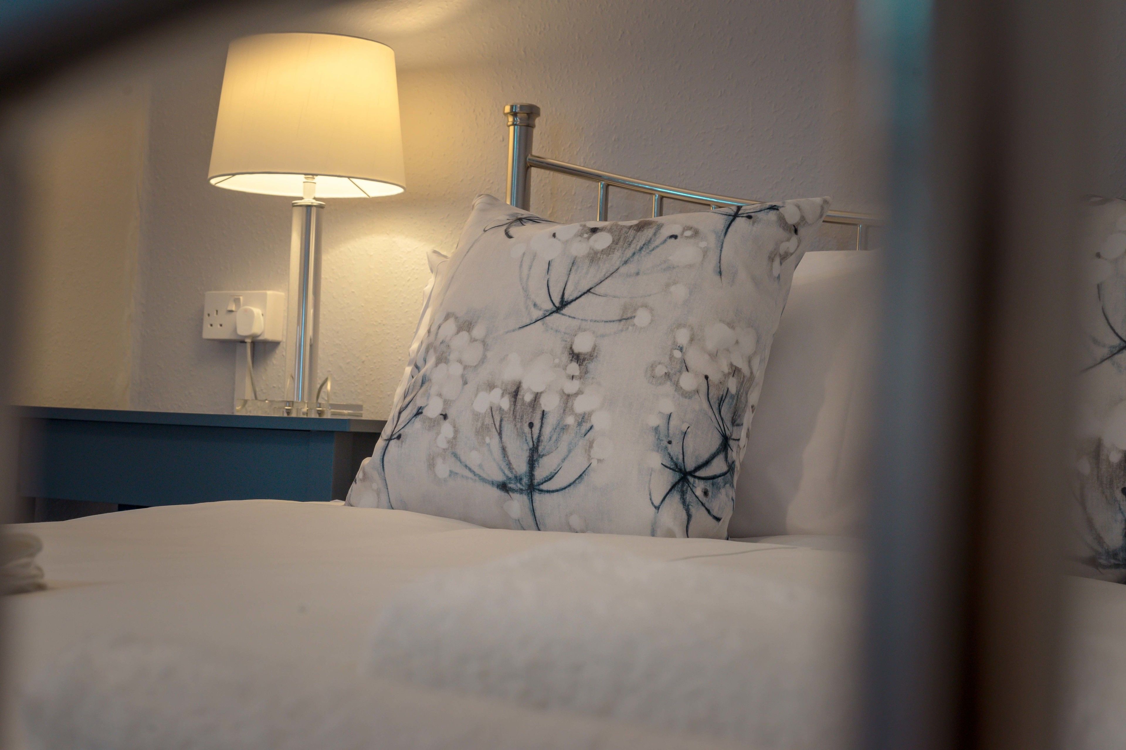 A hotel room with a bed, a nightstand, a lamp, and a wall socket.