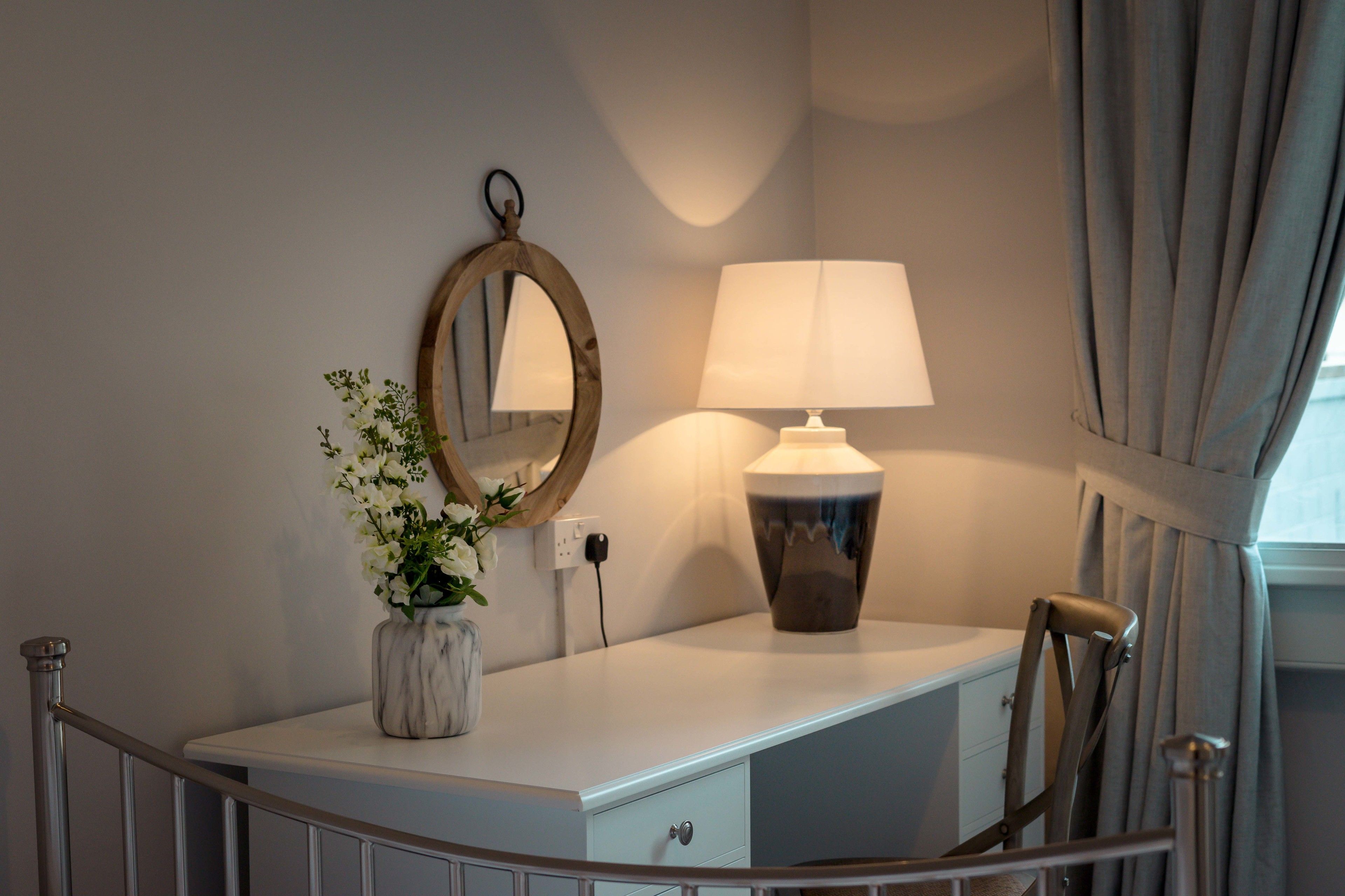 Un mobile bagno con specchio, una lampada e un vaso con fiori.