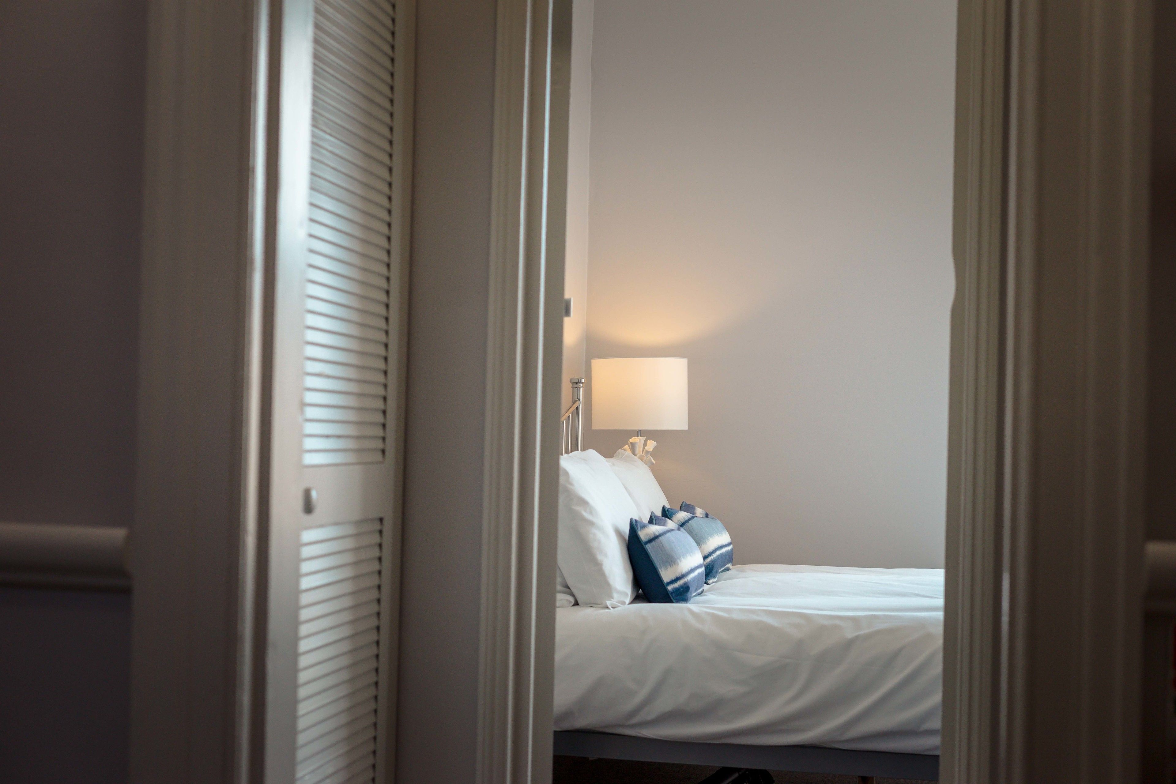 A hotel room with a bed, pillows, a lamp, and a window.