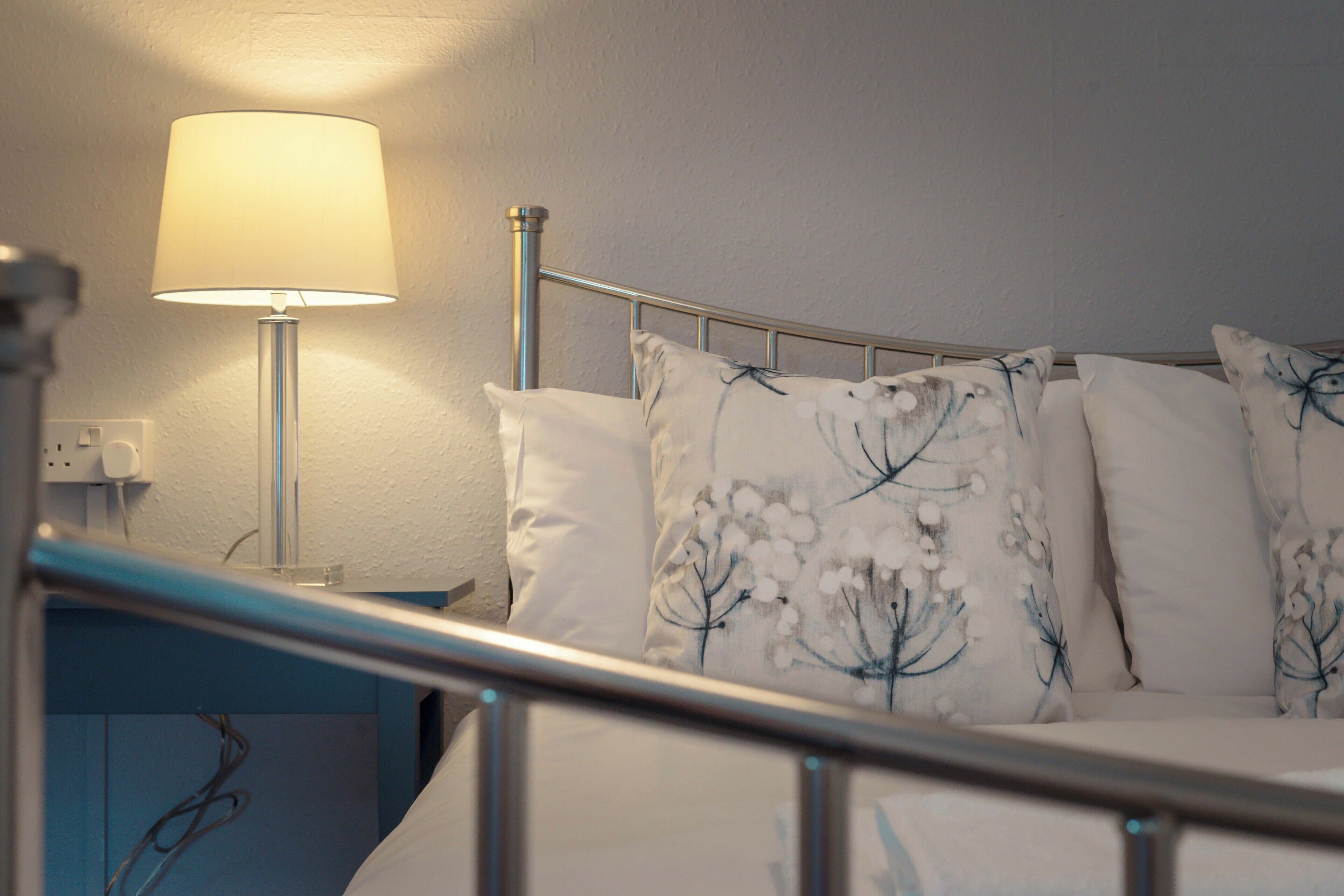 A neatly made bed with floral patterned pillows, a bedside lamp, and a metal headboard.