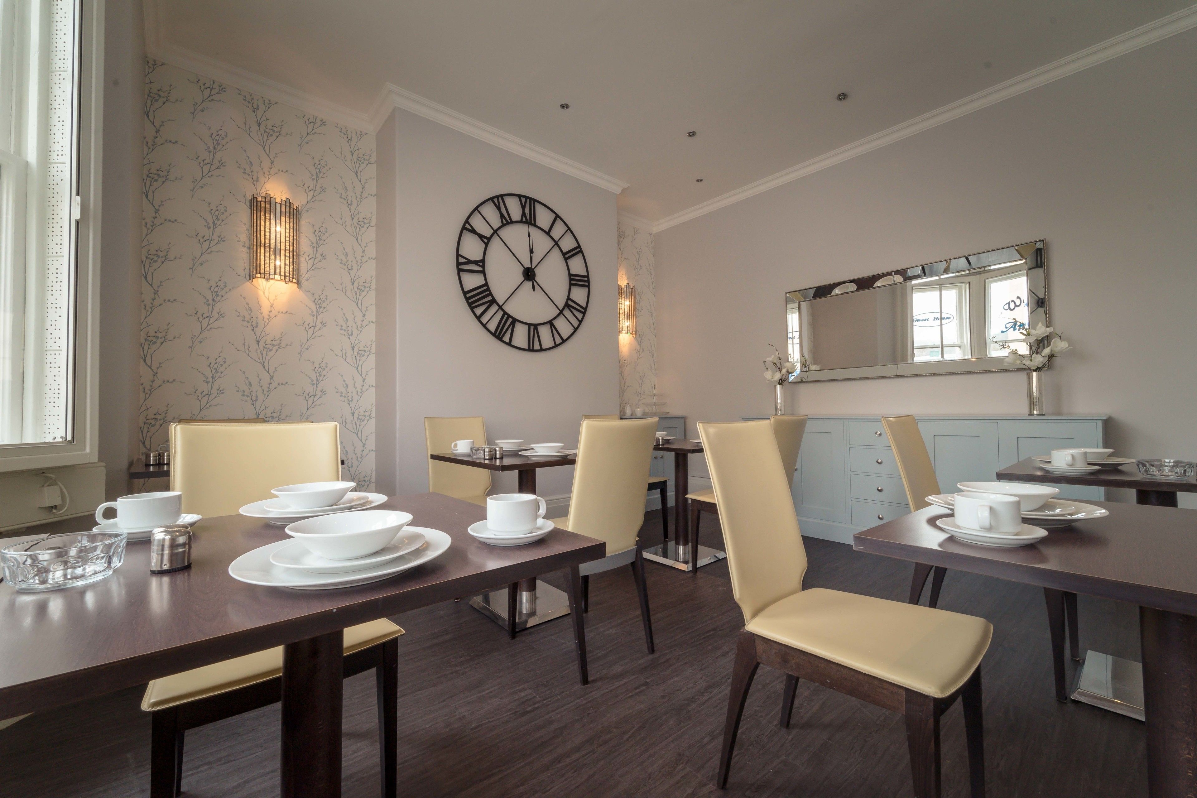 A dining area with a large wall clock, light fixtures, and a mirror above the counter.